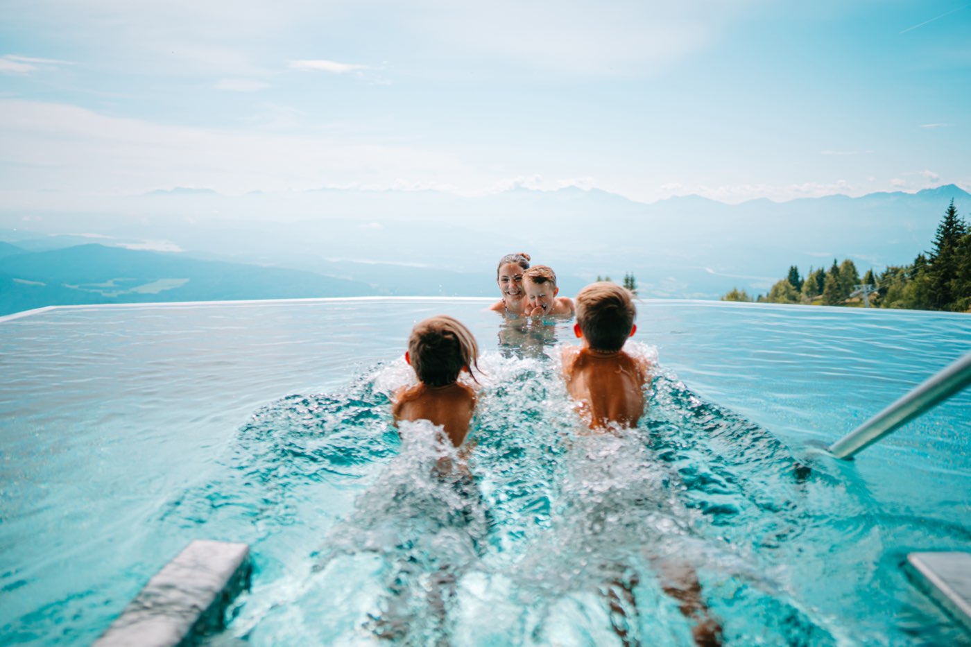 Zwei Kinder planschen im Skypool auf Mutter mit Kleinkind zu, dahinter das Tal