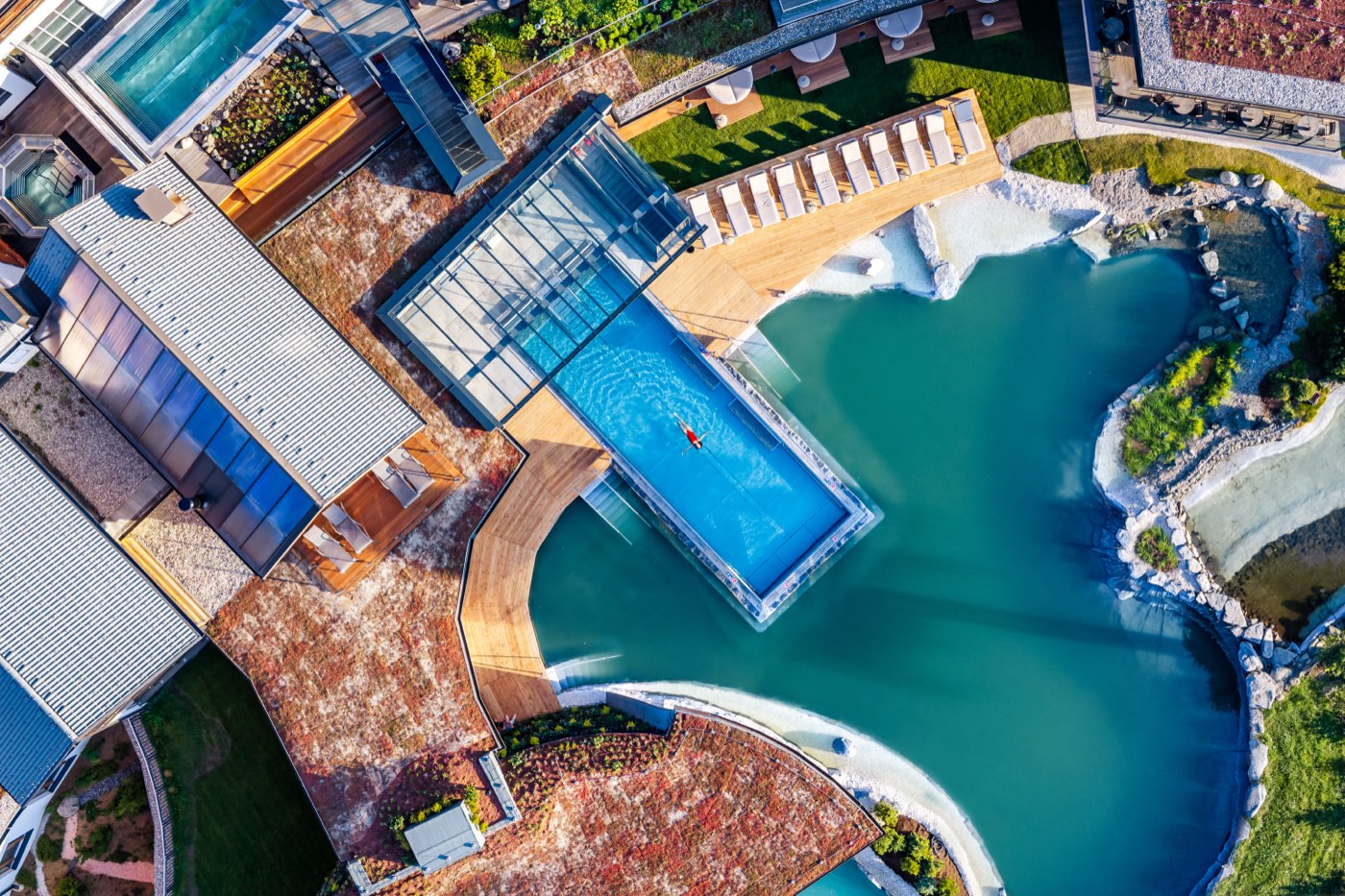 Luftbild senkrecht auf einen Pool mit Glasfront, der über den Naturbadeteich hinausragt